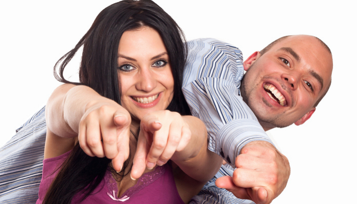 Portrait of happy young couple pointing at you over white background