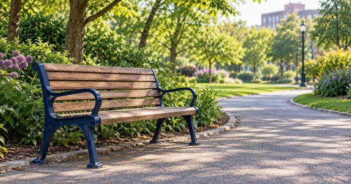An empty wooden bench with navy metal arms beside a paved path in a leafy neighborhood park.