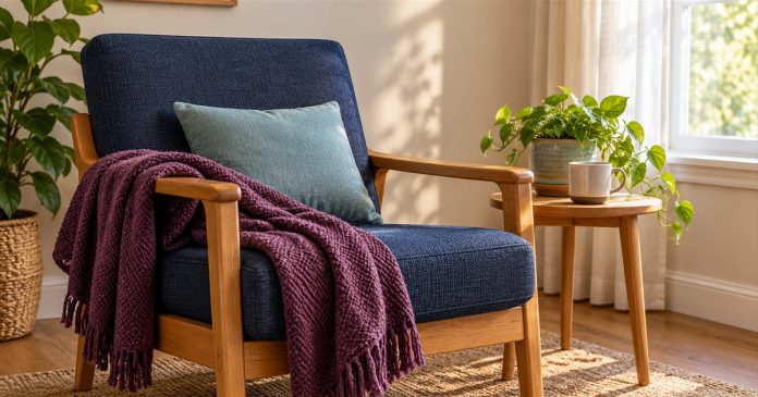 Indoor sensory grounding — chair, color and texture An empty navy armchair with a blue cushion and plum throw beside a sunlit window and small wooden table